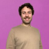 Photo of a man smiling against a pink background